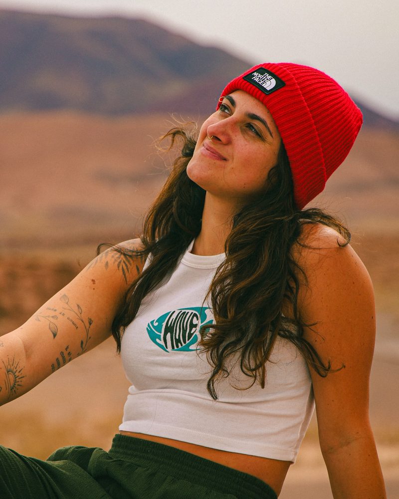Carol Cirillo, cofundadora da Pindó, sentada ao ar livre com gorro vermelho